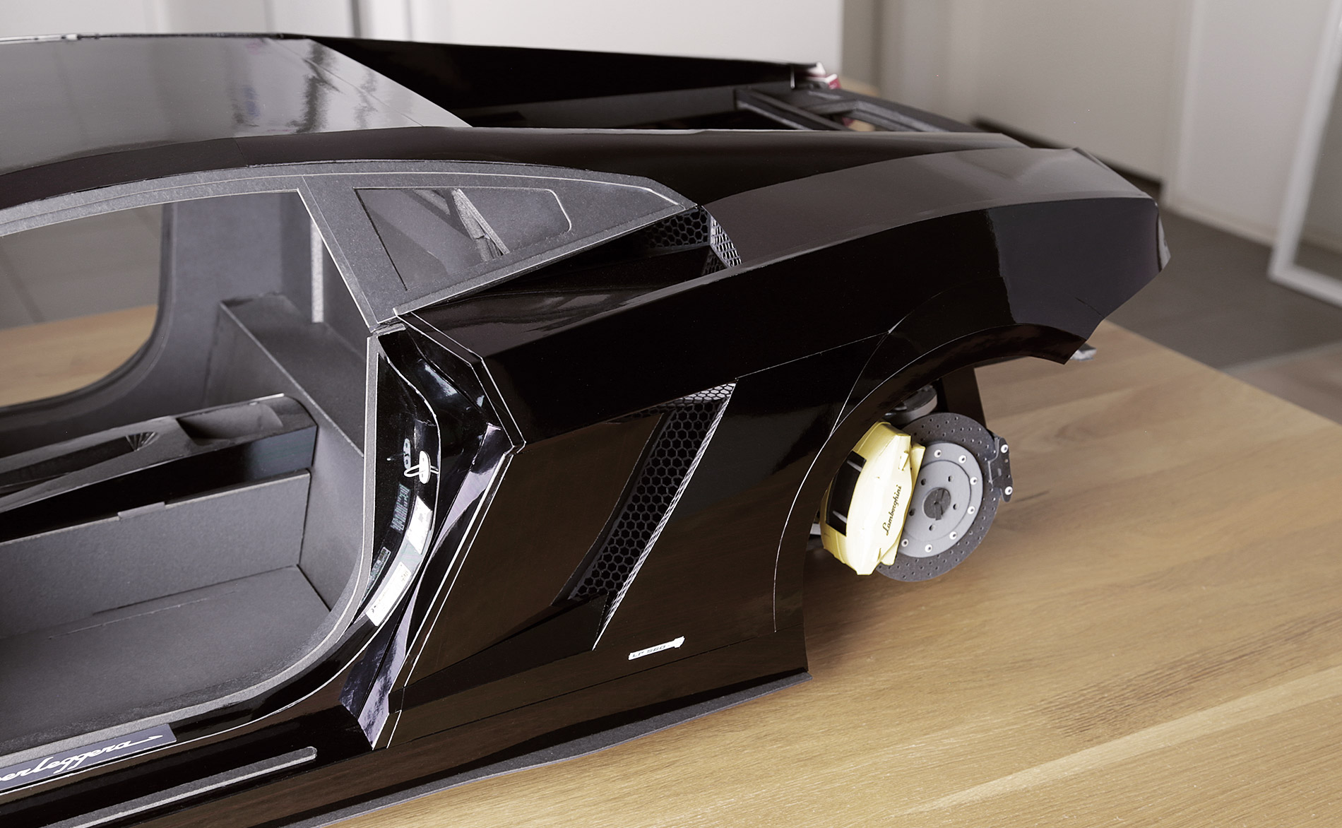 Rear fenders are complete. Outer body panels are cut from thin, shiny foil board. Mesh grills for oil cooler intake openings are hand cut from black paper. Tricky confluence of angles and surfaces in that door-jam area. Turned out great though.